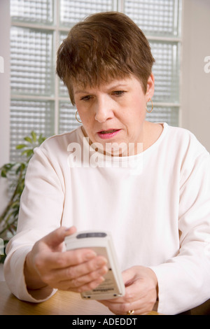 Mittlere gealterte Frau verbraucht Glukose-Monitor, um ihr Blutzuckerspiegel in ihrem Blut zu verfolgen. Stockfoto