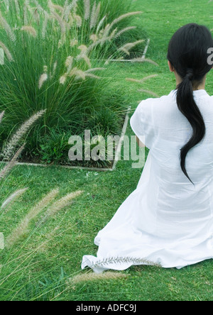 Frau sitzt auf dem gepflegten Rasen, Rückansicht Stockfoto