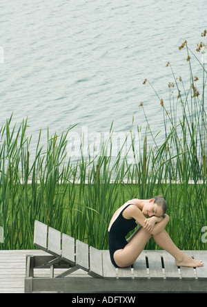 Frau sitzt auf Liegestuhl neben dem See, umarmt Knie, Kopf auf Arme ruhen Stockfoto