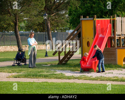 Mutter Eltern wacht über die Aufsicht über ihre zwei spielende Kinder Alter 2 und 6 auf einem Spielplatz in Peschiera del Garda Italien Stockfoto