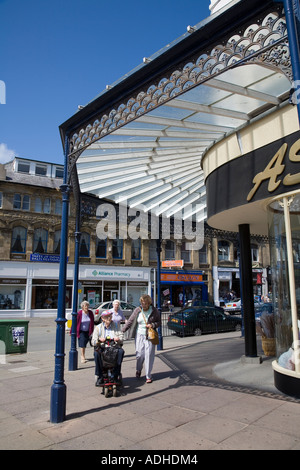 Älterer Mann auf motorisierten Rollstuhl unter viktorianischen Gehweg auf Ladenfront im shopping Straße Llandudno Wales UK Stockfoto