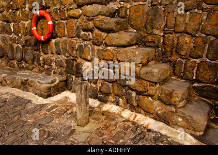 Alten Steintreppen auf das 14. Jahrhundert Hafenmauer in Clovelly mit einem hellen orange modernen Lebens-ring Stockfoto