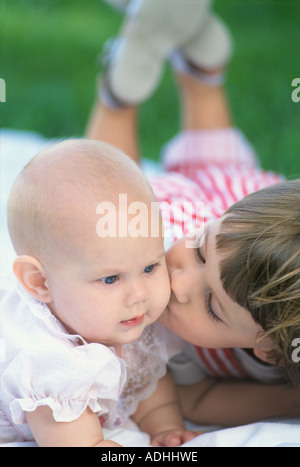 Junge Mädchen küssen Babyschwester auf Wange im Hinterhof Stockfoto