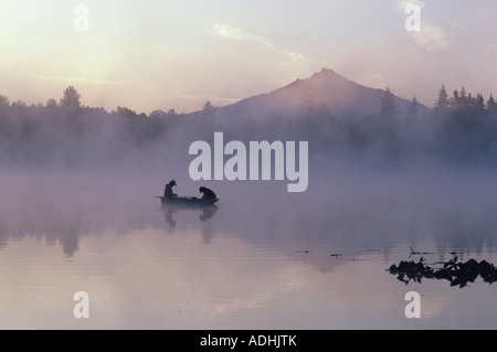 Sonnenaufgang am See Cassidy mit Mount Pilchuck im Nebel mit Silhouette Fischer in kleines Ruderboot Washington State USA Stockfoto