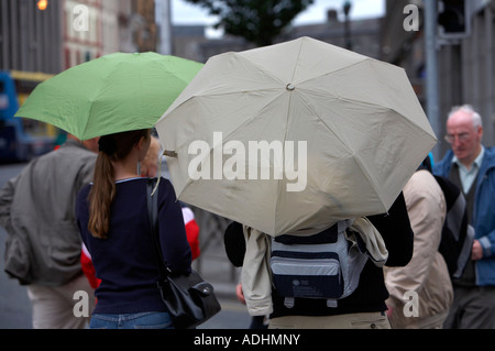Mann mit Rucksack und Frau mit Handtasche tragen Regenschirme, die darauf warten, überqueren Sie die Straße in dublin Stockfoto