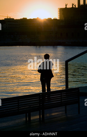Einsamer Mann in der Silhouette von der Wasserseite in Port Vell beobachten den Sonnenuntergang über Stadtzentrum von Barcelona Katalonien Spanien Stockfoto