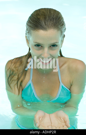Junge Frau im Pool stehend, in der Hand aus der hohlen Hand, lächelt in die Kamera Stockfoto