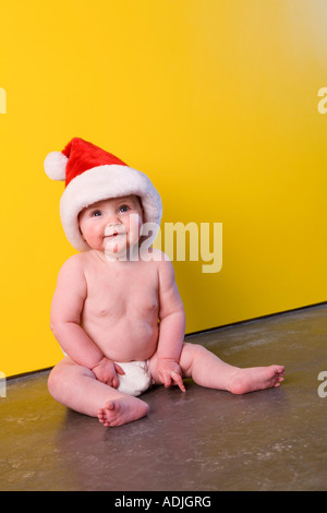 Porträt des Säuglings Mädchen tragen Weihnachtsmann Mütze sitzt auf Boden in Windel vor leuchtend gelbe Wand Winter Alaska Stockfoto