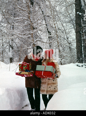 Saisonale Weihnachtsszene zeigt warm gekleidet, junger Mann und Frau, die Geschenke auf einem verschneiten Pfad Stockfoto