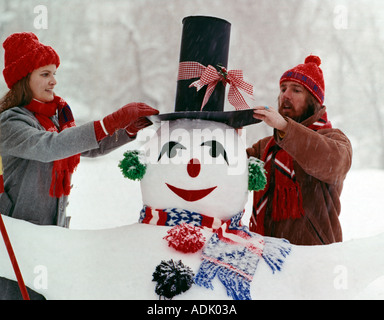 Junges Paar letzten Schliff auf einen lustigen Schneemann und Neuschnee fällt um sie herum Stockfoto