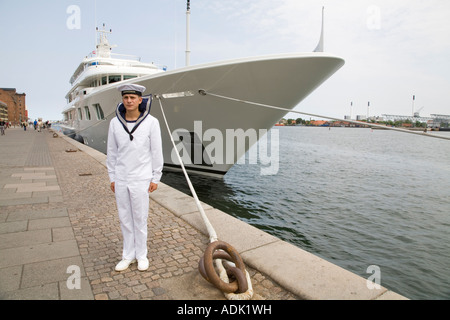 Ein junger Seemann steht um Aufmerksamkeit vor einer Luxusyacht im Hafen von Kopenhagen, Dänemark. Stockfoto