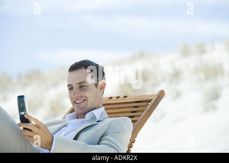 Geschäftsmann, sitzen im Liegestuhl am Strand, blickte auf Handy, Lächeln Stockfoto