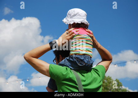 kleines Kind mit Sonnenhut auf Vaters Schultern sitzen Stockfoto