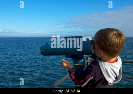 ein kleiner Junge, der Blick auf das Meer mit einem Teleskop in Penzance, Cornwall, england Stockfoto