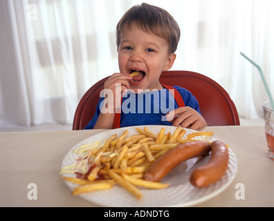 Kleiner Junge isst Pommes Frites und Würstchen mit mayonnaise Stockfoto