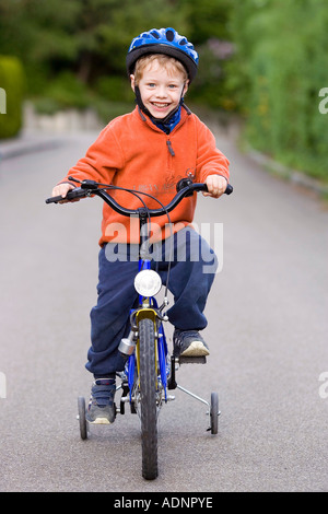 Kleiner Junge mit Bauarbeiterhelm auf seinem Fahrrad mit Stabilisatoren Stockfoto