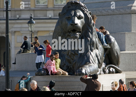 Touristen posieren für Fotos auf Löwenstatue an Basis von Nelson s Spalte Trafalgar Square in London UK Stockfoto