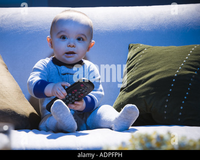 Baby auf Sofa mit TV-Fernbedienung Stockfoto