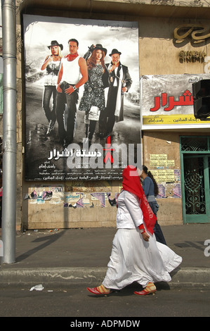 Eine ägyptische Frau das Tragen eines traditionellen Abaya Kleidungsstück Spaziergang, vorbei an einem Film Plakat in Heliopolis Ägypten Stockfoto