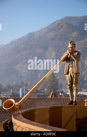 Mann im bayerischen Kleidung spielt Alphorn auf Balkon Sims im Hotel Enzian in Leavenworth, Washington Stockfoto