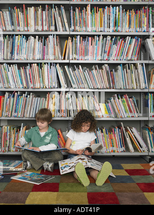 Jungen und Mädchen sitzen auf dem Boden der Bibliothek Bücher zu lesen Stockfoto