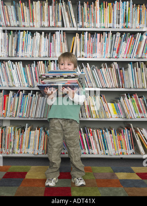 Junge hält Stapel Bücher vor Bibliothek Bücherregal Stockfoto