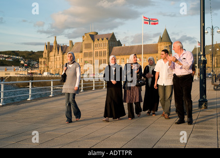 Gruppe von muslimischen Männern und Frauen zu Fuß in Aberystwyth Promenade mit der University of Wales Old College Gebäude hinter im Gespräch Stockfoto