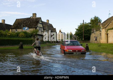 Auto und junge auf einem Fahrrad versuchen, durch Hochwasser in Minster Lovell Oxfordshire England Vereinigtes Königreich bewegen Stockfoto