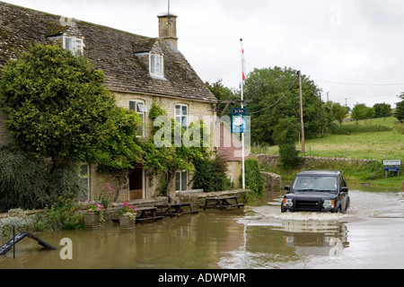 Mit dem Geländewagen fahren Auto fährt durch überflutete Straße in Swinbrook Oxfordshire in England Vereinigtes Königreich Stockfoto