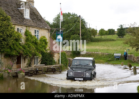 Mit dem Geländewagen fahren Auto fährt durch überflutete Straße in Swinbrook Oxfordshire in England Vereinigtes Königreich Stockfoto