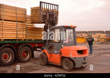 EINE GABELSTAPLER HEBT HOLZ FECHTEN BEITRÄGE AUF EINES SATTELSCHLEPPERS AUF DAS DOCKSIDE EINEN HAFEN IN NEWPORT SOUTH WALES UK Stockfoto