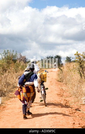 Ein Black Muslim-paar treibt ein Fahrrad auf einem Feldweg im Norden Mosambiks unter blauem Himmel mit geschwollenen weiße Wolken gefüllt Stockfoto