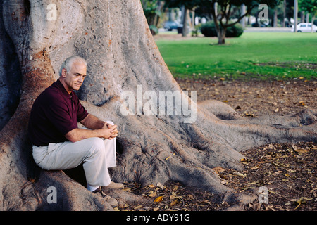 Mann, sitzend auf Basis des Baumes Stockfoto
