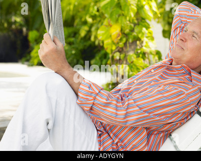 Mann liegend auf Lounge Stuhl lesen Zeitung, Seitenansicht Stockfoto