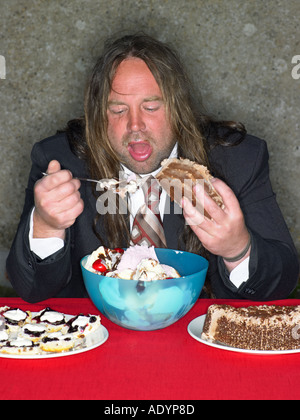 Langhaarige dicker Mann stopft sich mit Kuchen und Eis essen Stockfoto