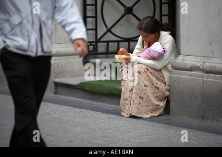 Junge Zigeunerin beggar woman holding, was aussieht wie ein Baby in Decke essen Chips in Tür als Mann Vergangenheit Oconnell Street Dublin gewickelt Stockfoto