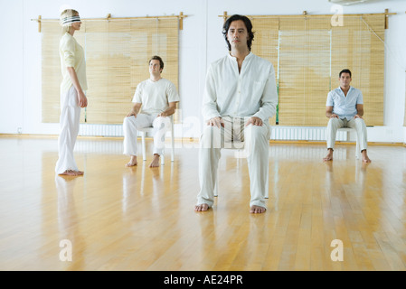 Gruppentherapie, Augenbinde Erwachsene sitzen auf Stühlen, während eine Frau steht, trägt Stockfoto