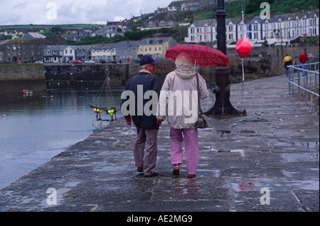 Älteres Ehepaar zu Fuß entfernt von der Kamera bei nassem Wetter mit Regenschirm Porthleven Cornwall England Stockfoto