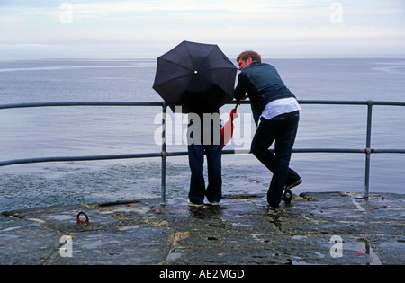Junges Paar mit Regenschirm bei Regenwetter Blick auf das Meer vom Ende eines Piers Stockfoto