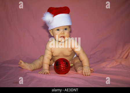 Porträt von einem 4 Monate Babymädchen einen Weihnachtsmann Hut mit einer Christbaumkugel Stockfoto