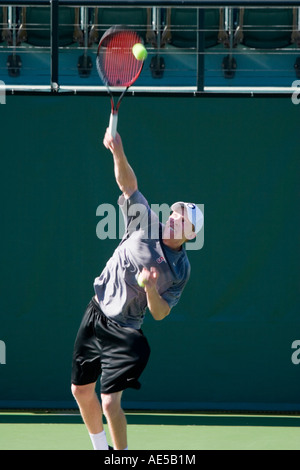 Mann in seinen 20ern Strecken sich mit seinen Schläger zu treffen und einen gelben Tennisball auf einem Tennisplatz zu dienen Stockfoto