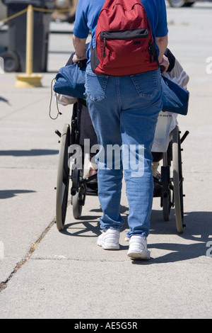 Eine Frau in Jeans zurückschieben einen Mann im Rollstuhl Stockfoto