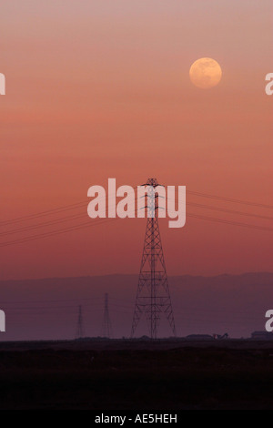 Mond steigt über die Silhouette des Power Towers und Stromleitungen vor einem rosa Sonnenuntergang Himmel Redwood City, Kalifornien Stockfoto