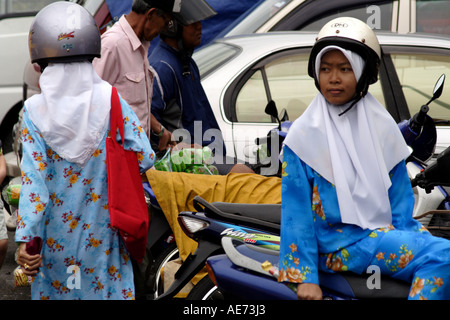 Muslimische Frauen mit Motorradhelme über traditionelle Kopf bedecken außerhalb des Marktes, Kuching, Sarawak, Borneo, Malaysia Stockfoto