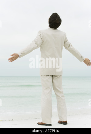 Geschäftsmann am Strand mit Armen, Rückansicht Stockfoto