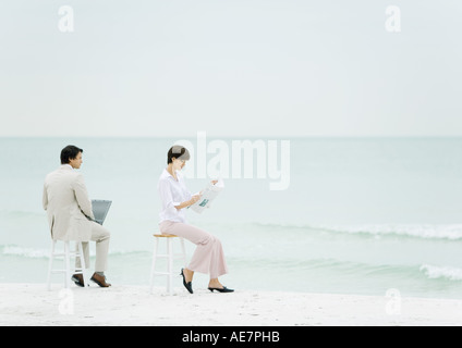 Geschäftsleute, die sitzen auf Hockern am Strand, mit Laptop, eine andere Lesart Zeitung Stockfoto