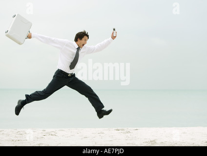 Geschäftsmann, laufen und springen am Strand Stockfoto