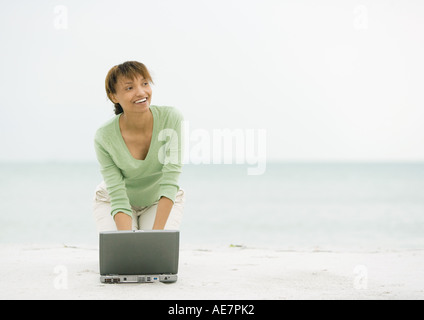 Frau am Strand, kniend auf Sand mit laptop Stockfoto