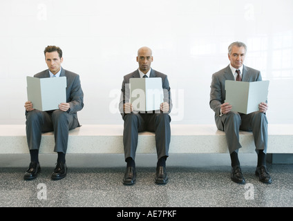 Drei Männer in Anzügen sitzen auf Bank und hält Ordner öffnen Stockfoto