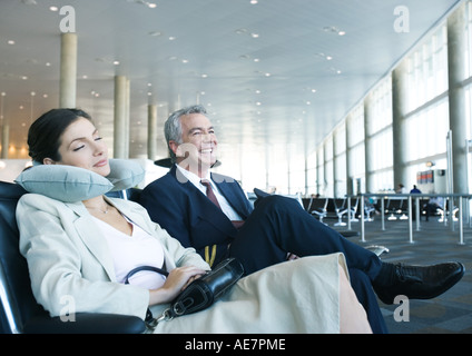 Geschäftsreisende, die sitzen in Flughafen-Lounge, ein Nickerchen mit Nackenkissen neben lächelnd Mann Frau Stockfoto